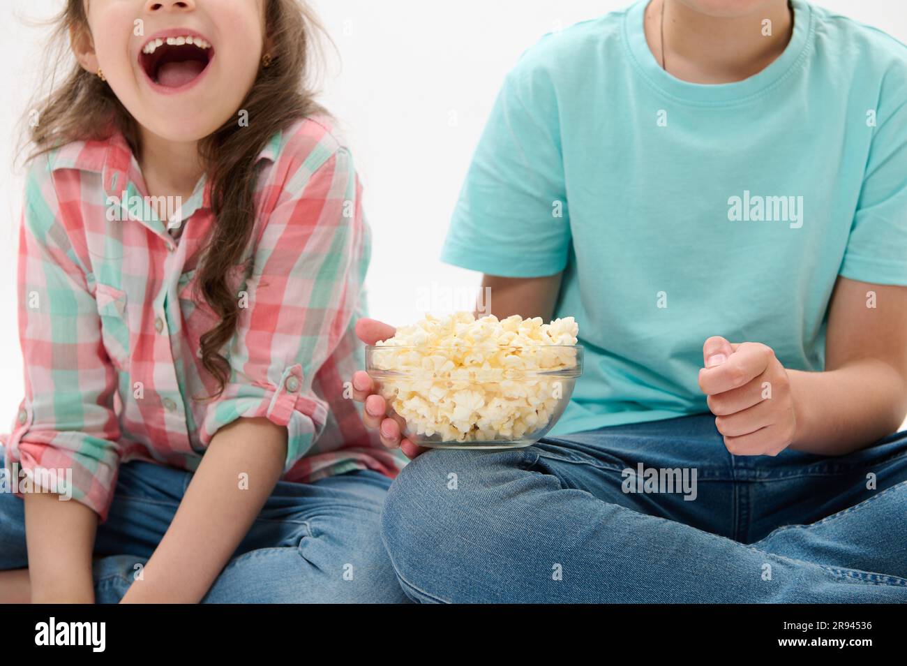 Details on a bowl of popcorn in the hands of cute children watching movies or cartoons over white isolated background Stock Photo