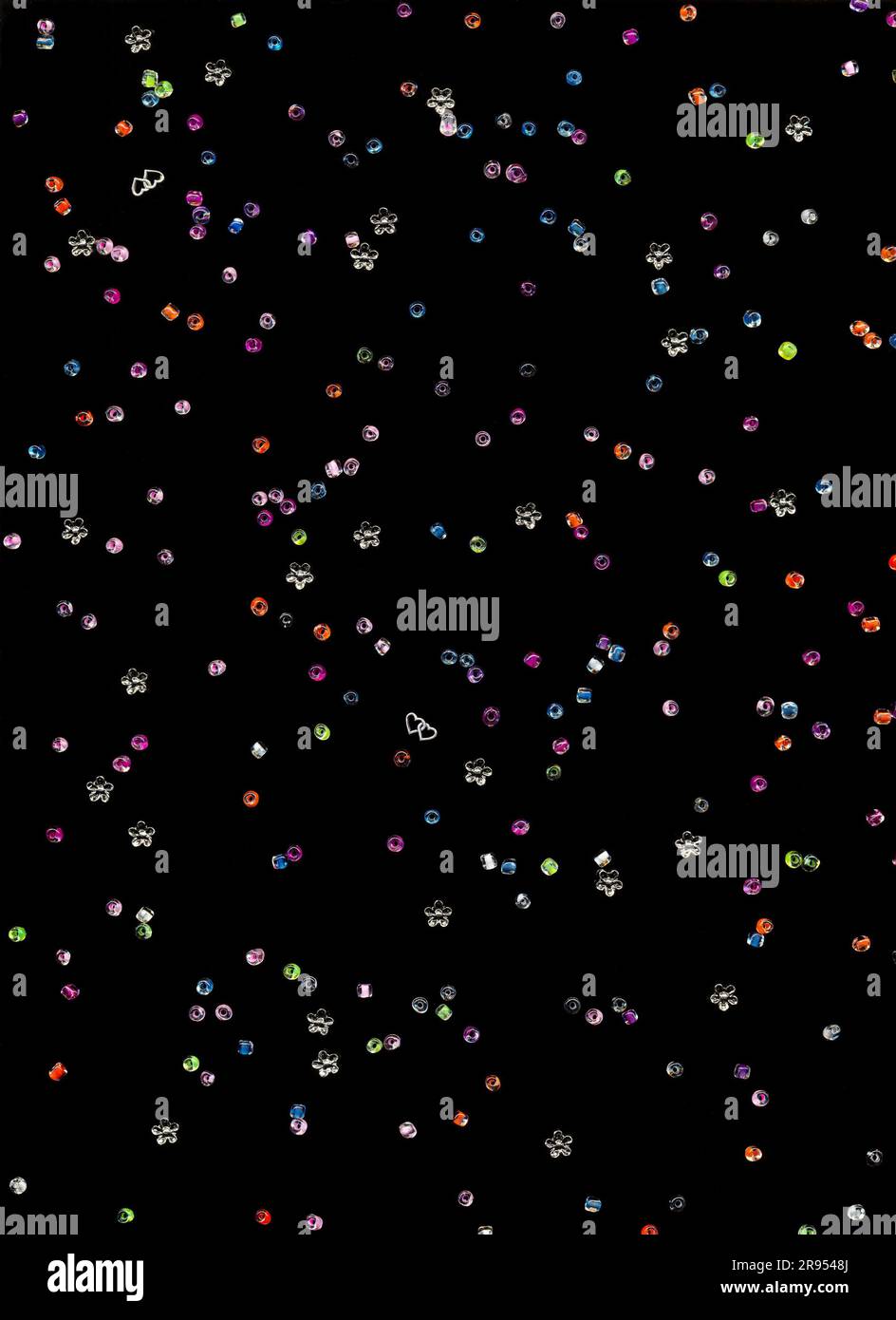 Colorful glass and flower beads scattered on a black background, top view. Craft supply for kids hobby of making jewelry - Stock Image