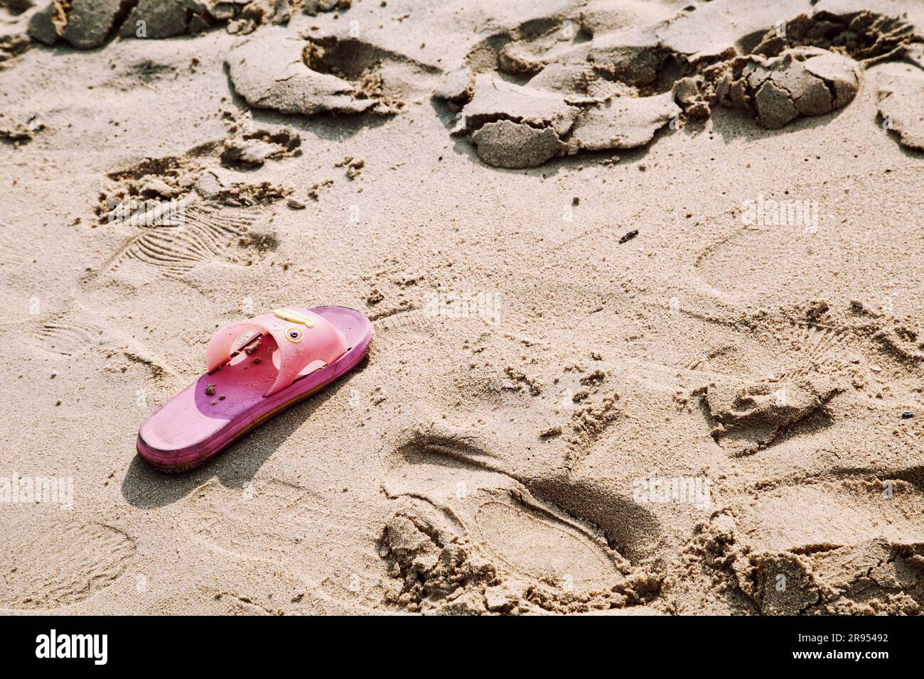 One ink rubber slipper lost at a beach. Adult plastic shoe without a pair abandoned in the sand. Missing person concept - Stock Image