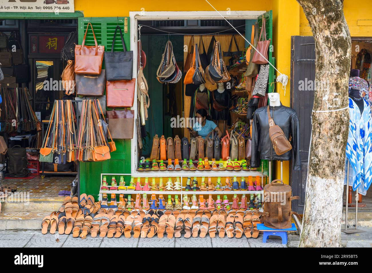 Local shopkeeper looks at her mobile phone inside her leather goods shop in old town Hoi An, Vietnam. Stock Photo
