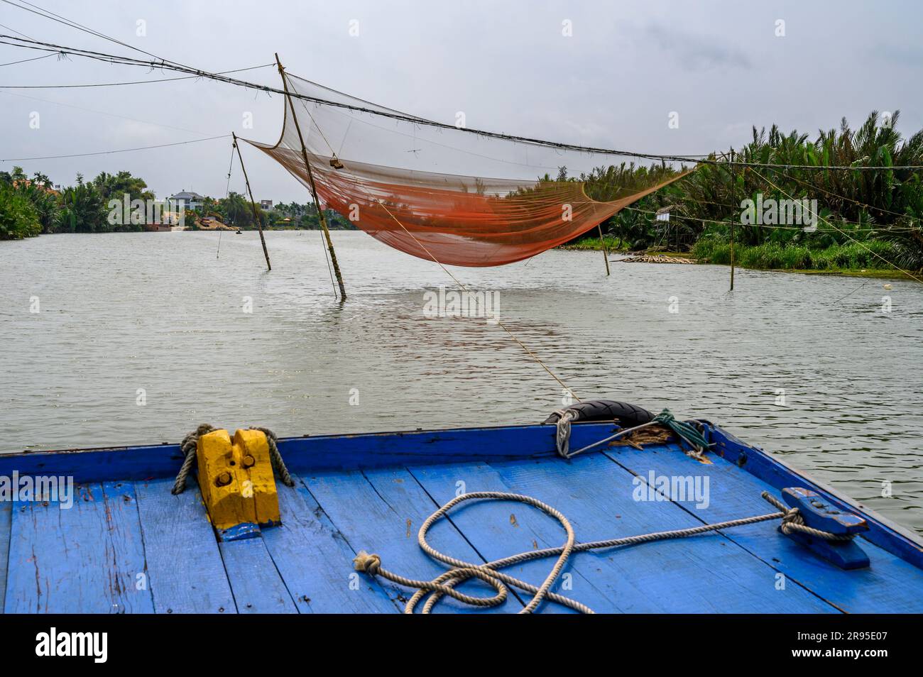 A blue wooden boat sails downstream on Thu Bon river on its way from Hoi An  market to Red Bridge Cooking School passing a fishing net. Vietnam Stock  Photo - Alamy