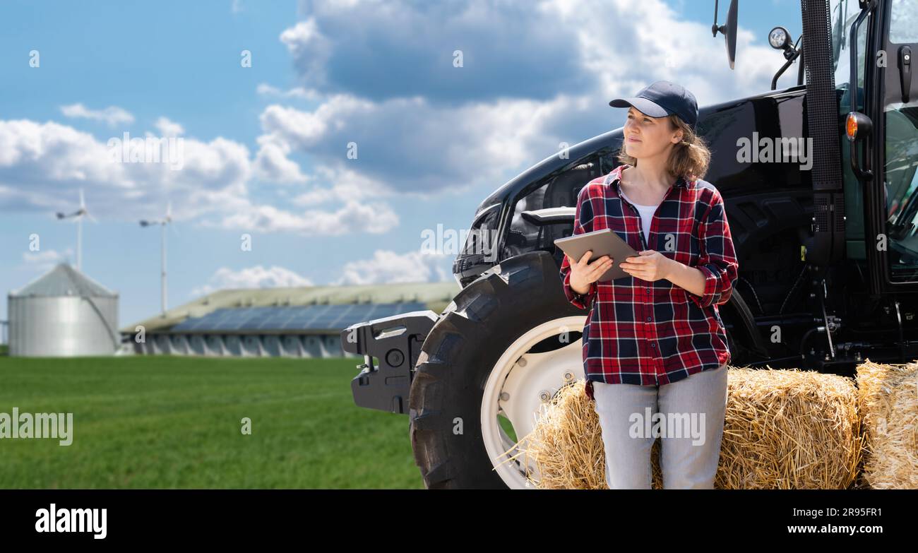 Woman farmer with a digital tablet and agricultural tractor on a background of modern farm. Stock Photo