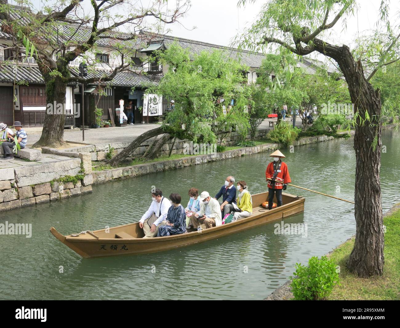 A boatman in traditional costume takes tourists in a punt along the canal in Kurashiki, past the old rice warehouses of the Bikan historical area. Stock Photo