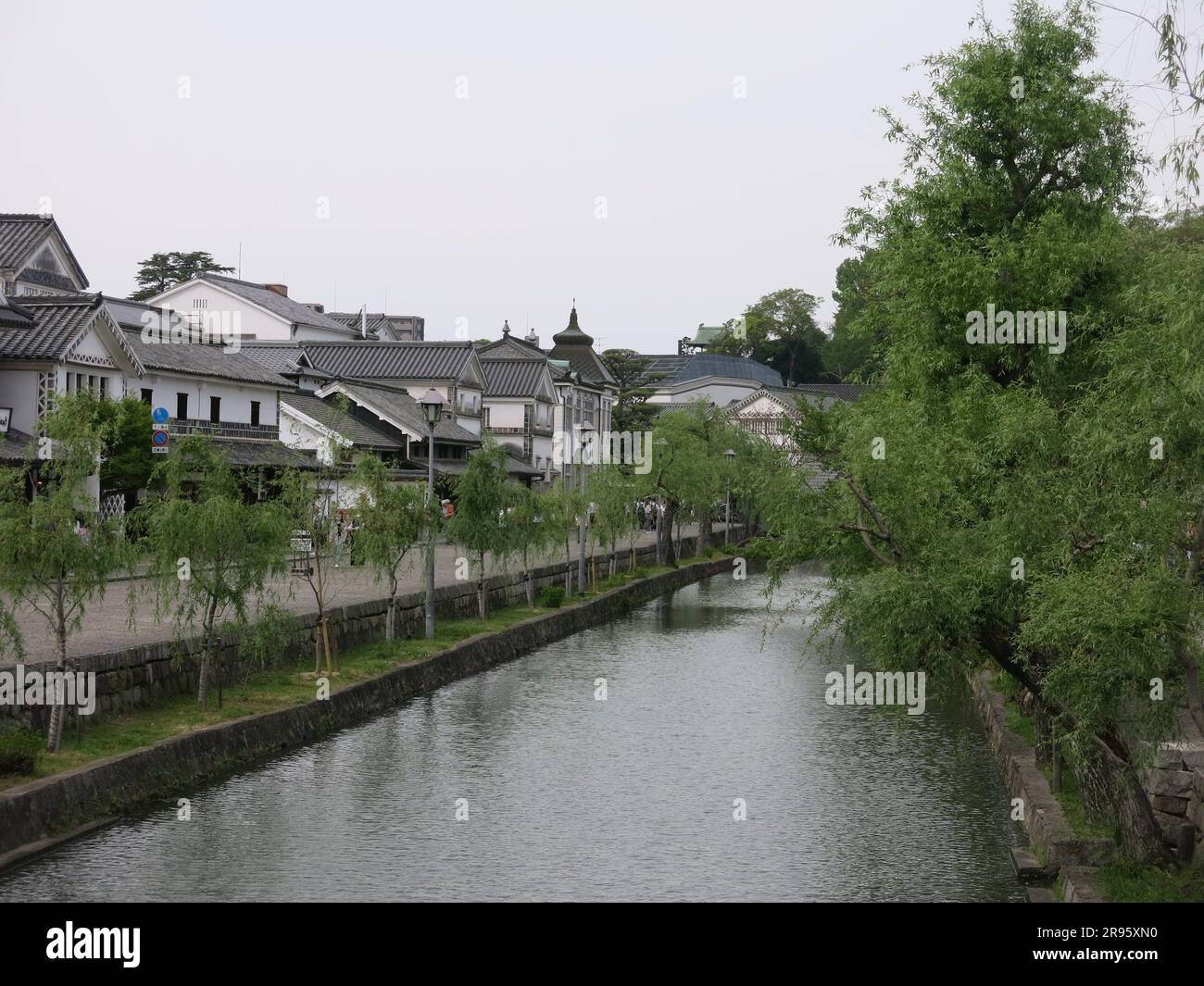 Kurashiki has a preserved canal area with the old rice warehouses painted white with black tiles, and weeping willows lining the waterside. Stock Photo