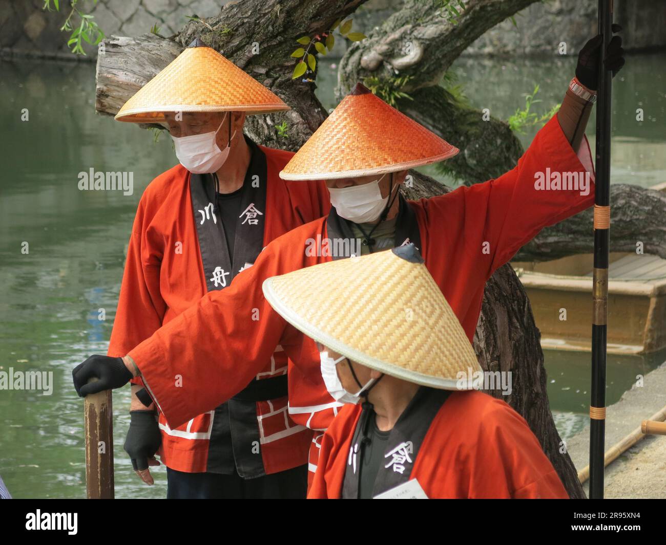 A trio of boatmen in traditional dress with conical straw hats await at the side of the canal in Kurashiki to take tourists on a leisurely punt. Stock Photo