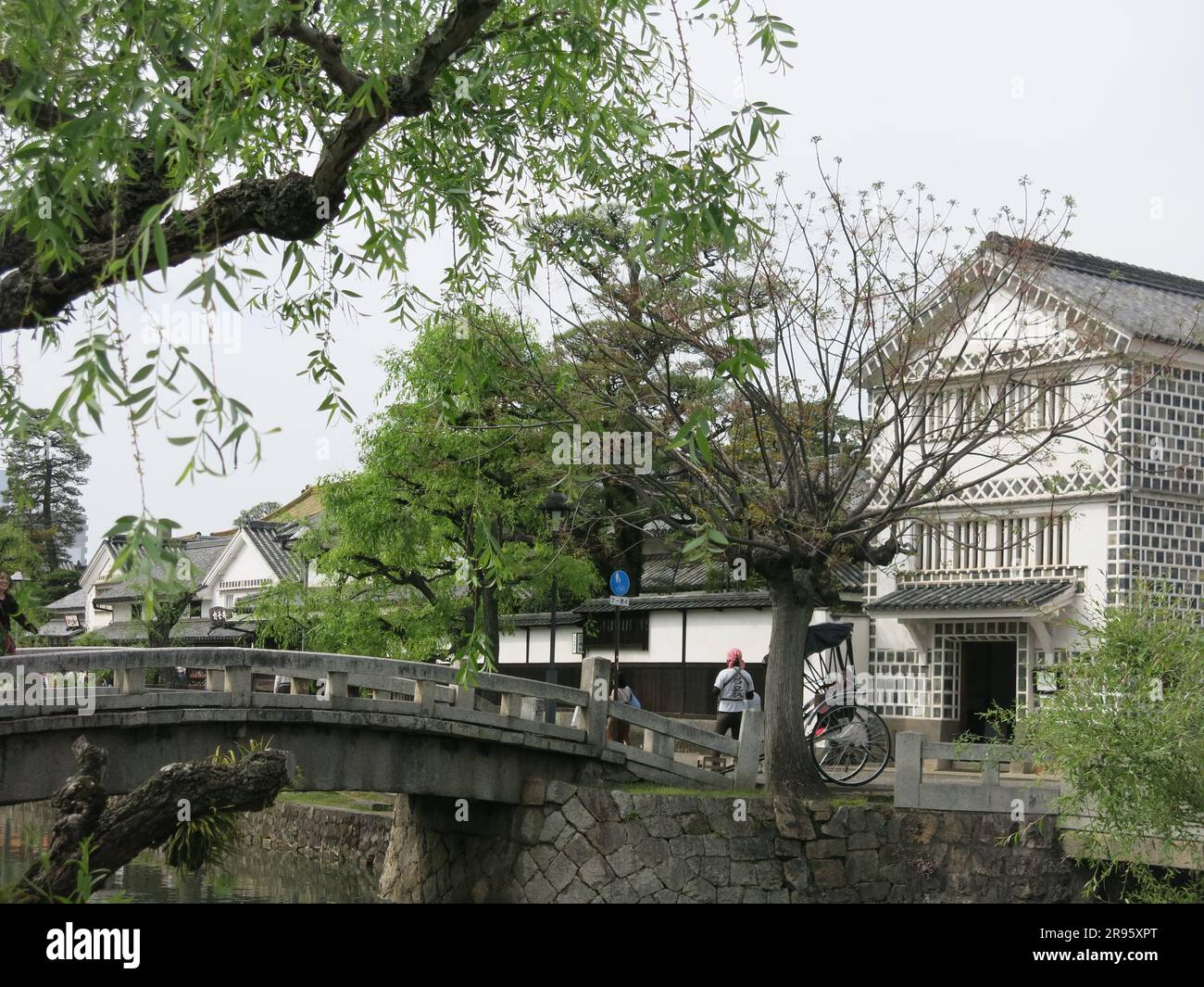 Kurashiki has a preserved canal area with the old rice warehouses painted white with black tiles, and weeping willows lining the waterside. Stock Photo