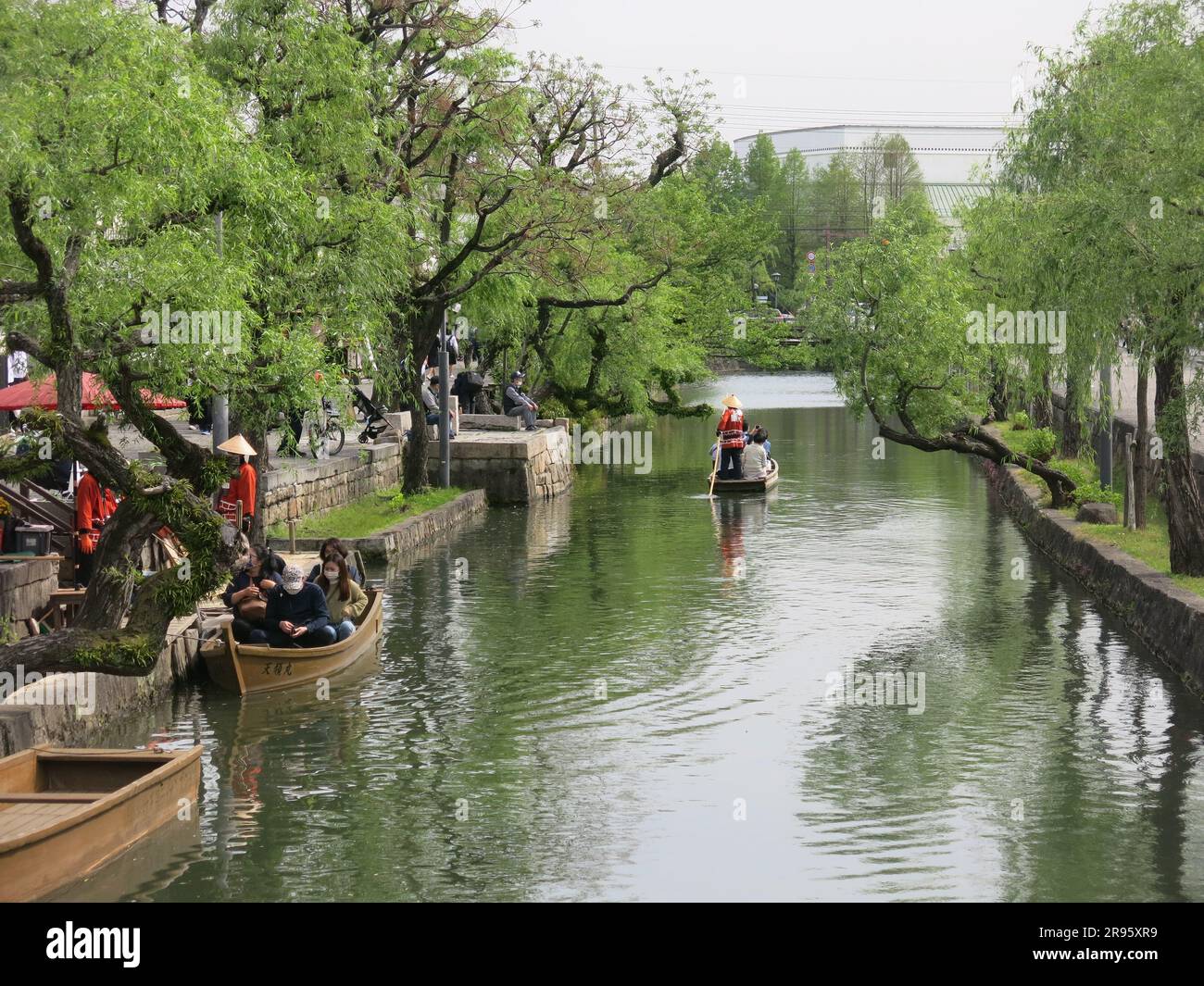 Punts with boatmen in traditional costume provide a leisurely sail along the canal for tourists to the quaint old town of Kurashiki, Japan. Stock Photo