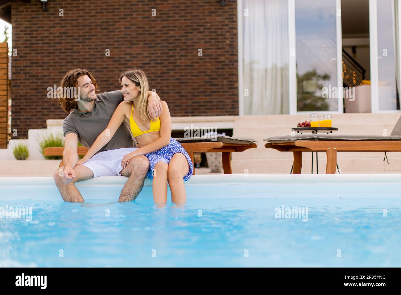 Handsome young couple relaxing by the swimming pool in the house ...