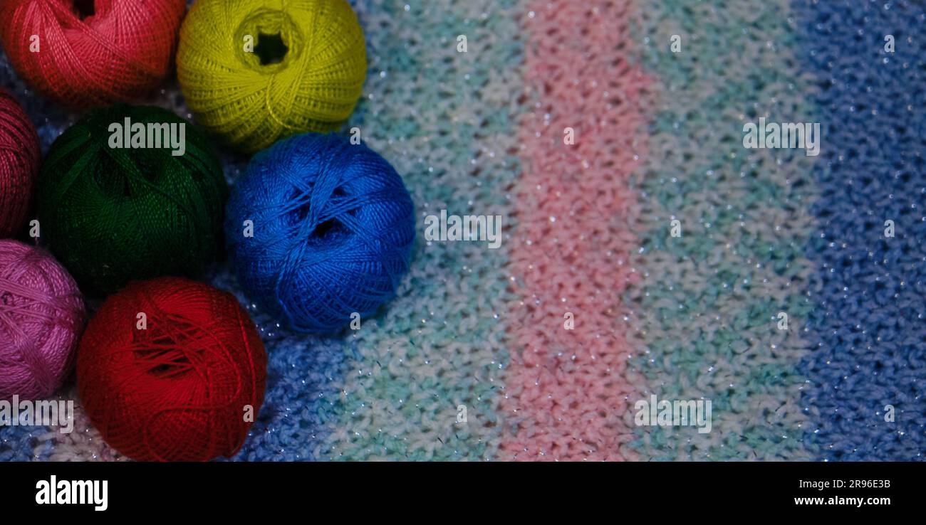 Yarn for crocheting. Several woolen multicolored balls of thread on striped pink blue crocheted background. Concept hobby of handmade needlework from Stock Photo