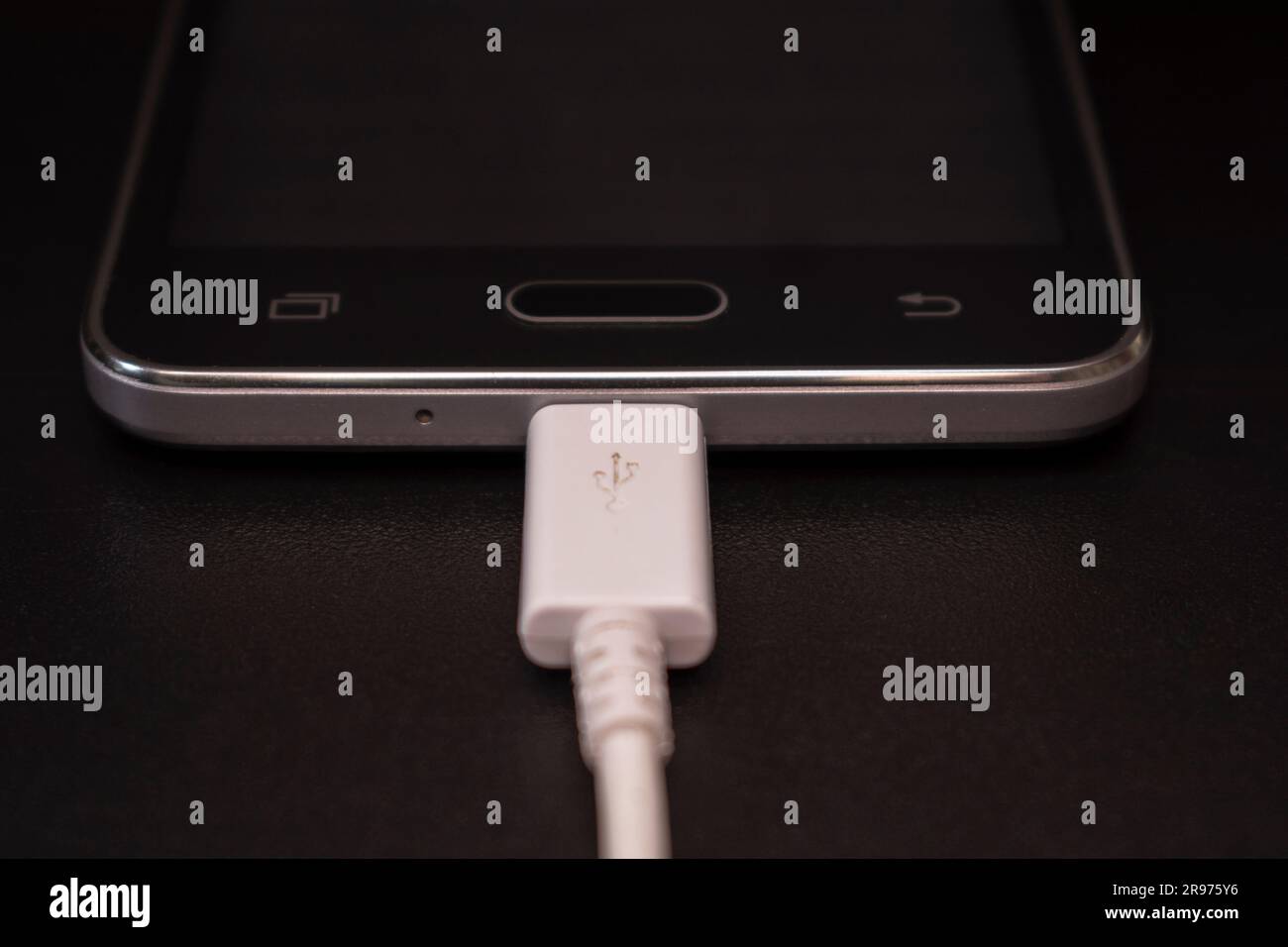 black smartphone on a black matte background with a white connected cable Stock Photo