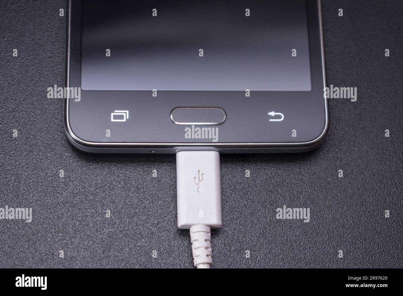 black smartphone on a black matte background with a white connected cable Stock Photo