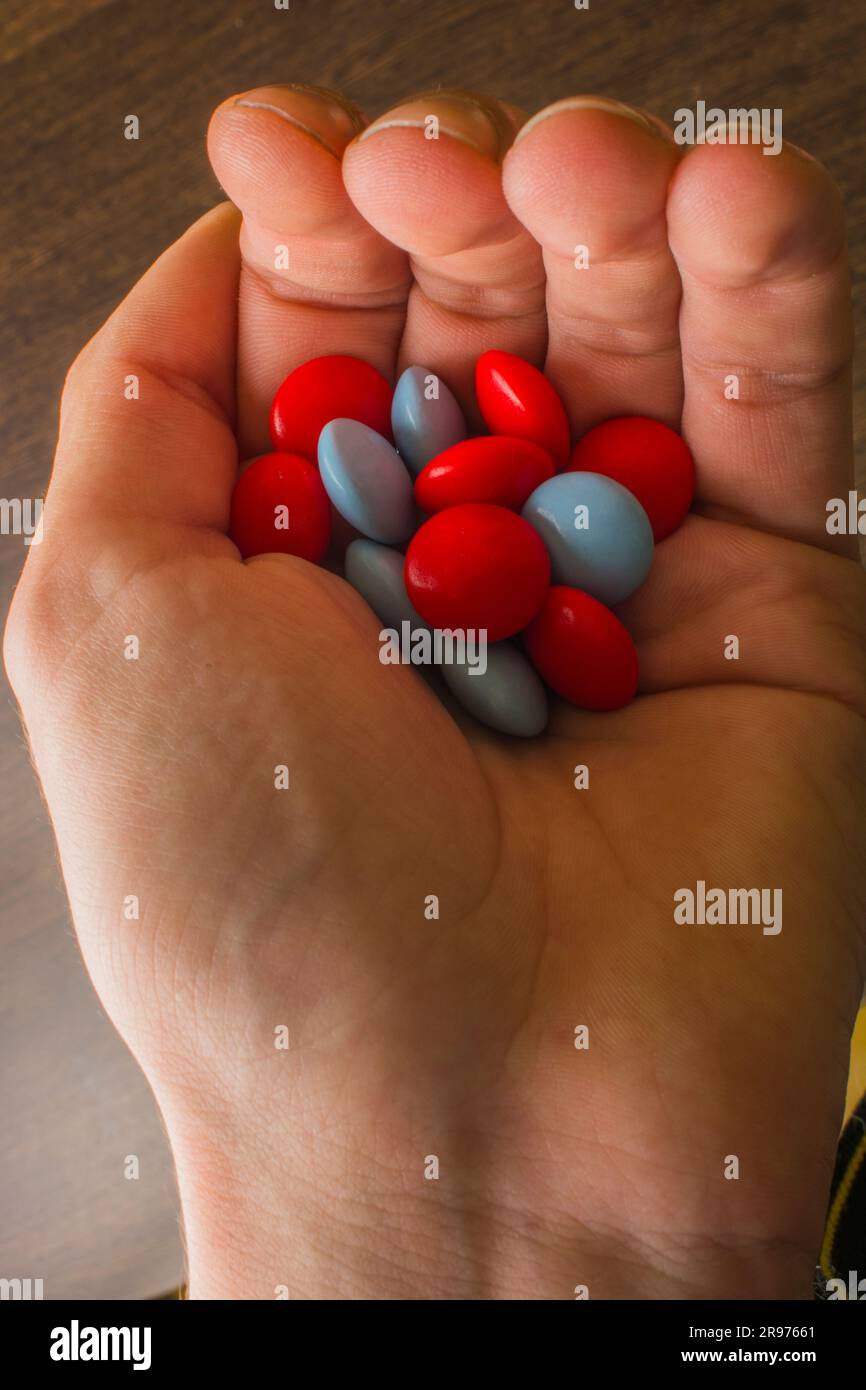 red and blue tablets in hand on the background of a wooden table Stock Photo