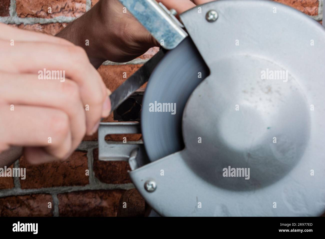 A knife sharpener and hand with a blade on a wooden table, close-up against a brick wall background Stock Photo
