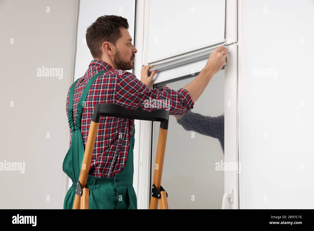 Worker in uniform installing roller window blind indoors Stock Photo