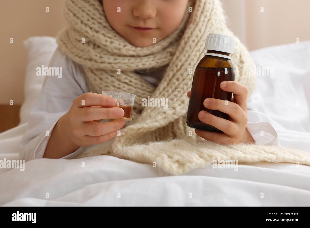 Sick girl taking cough syrup on bed at home, closeup. Cold medicine