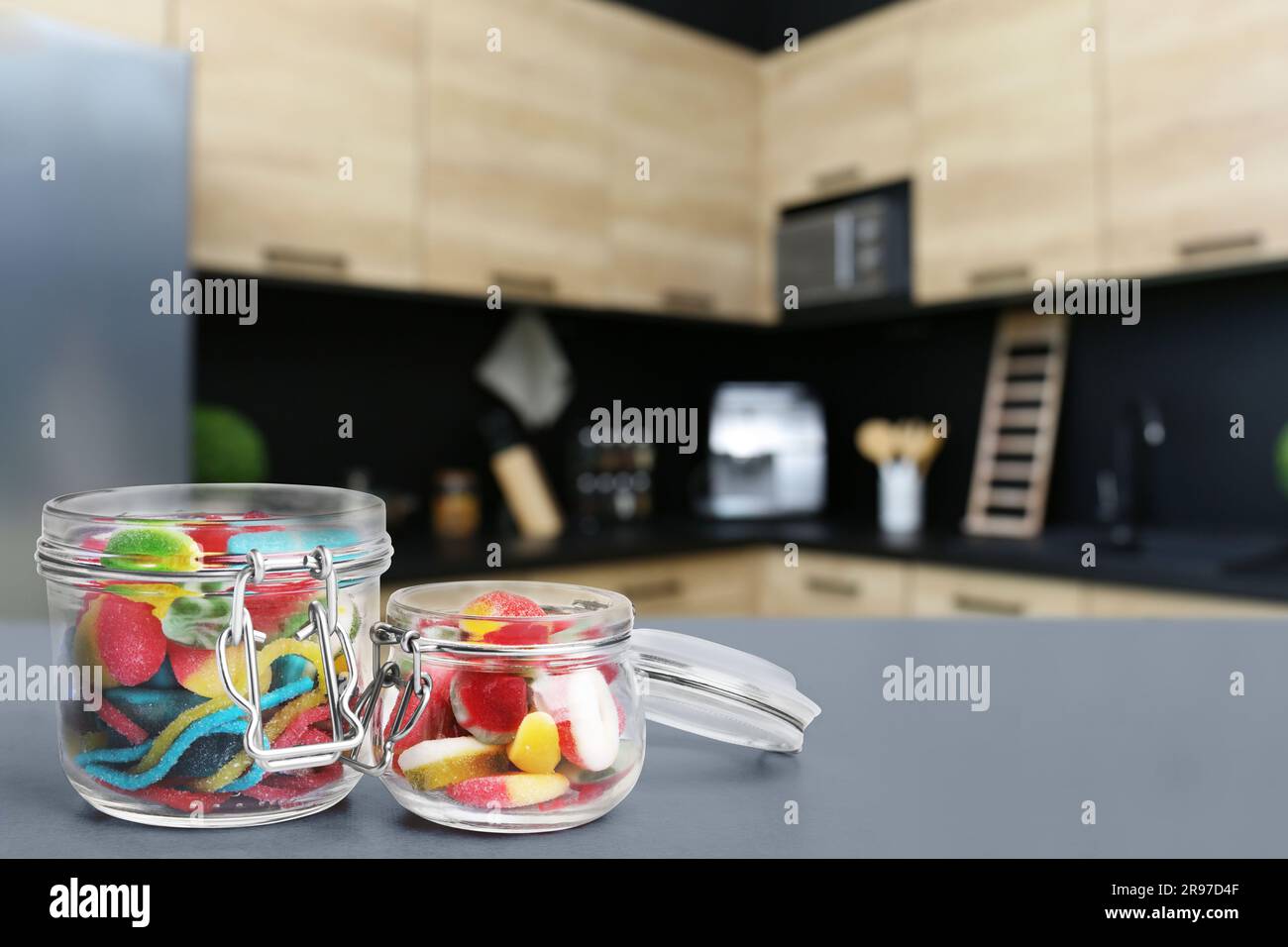 Glass jars with tasty gummy candies on grey table in kitchen. Space for