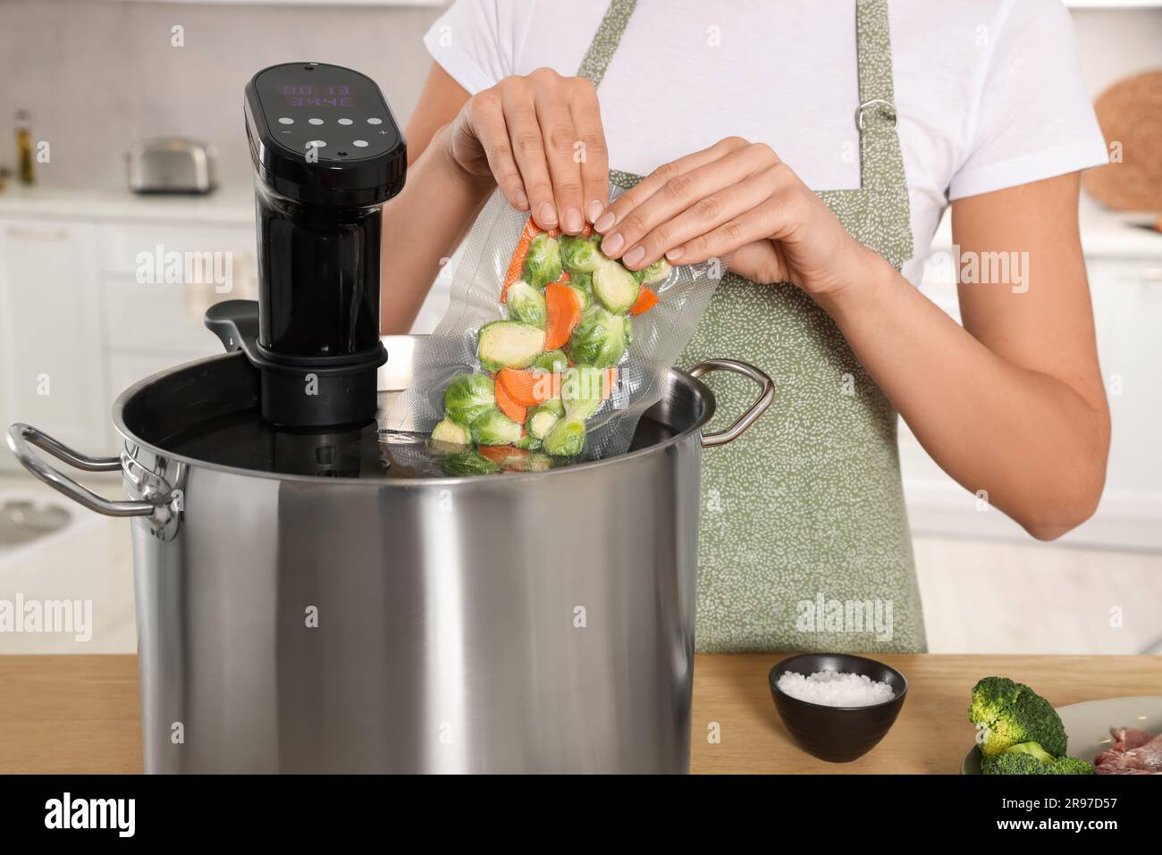 Woman putting vacuum packed vegetables into pot with sous vide cooker