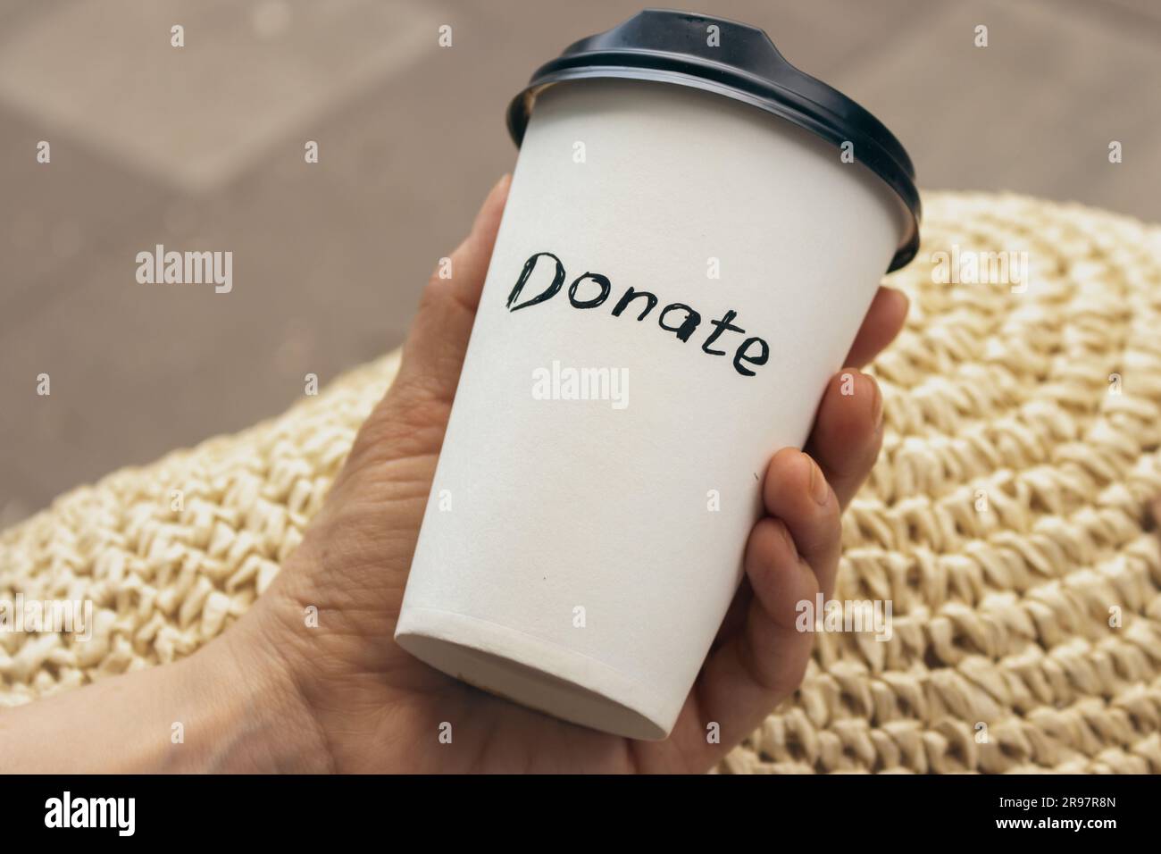 White cup with text Donate in hand. Charity concept. Hand holding cup of coffee take away. Donate logo on paper cup. Donation concept. Social activity Stock Photo