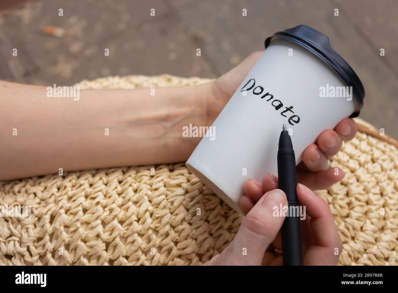 Woman drawing word donate on white cup. Charity concept. Hand holding cup of coffee take away. Donate logo on paper cup. Donation concept. Stock Photo