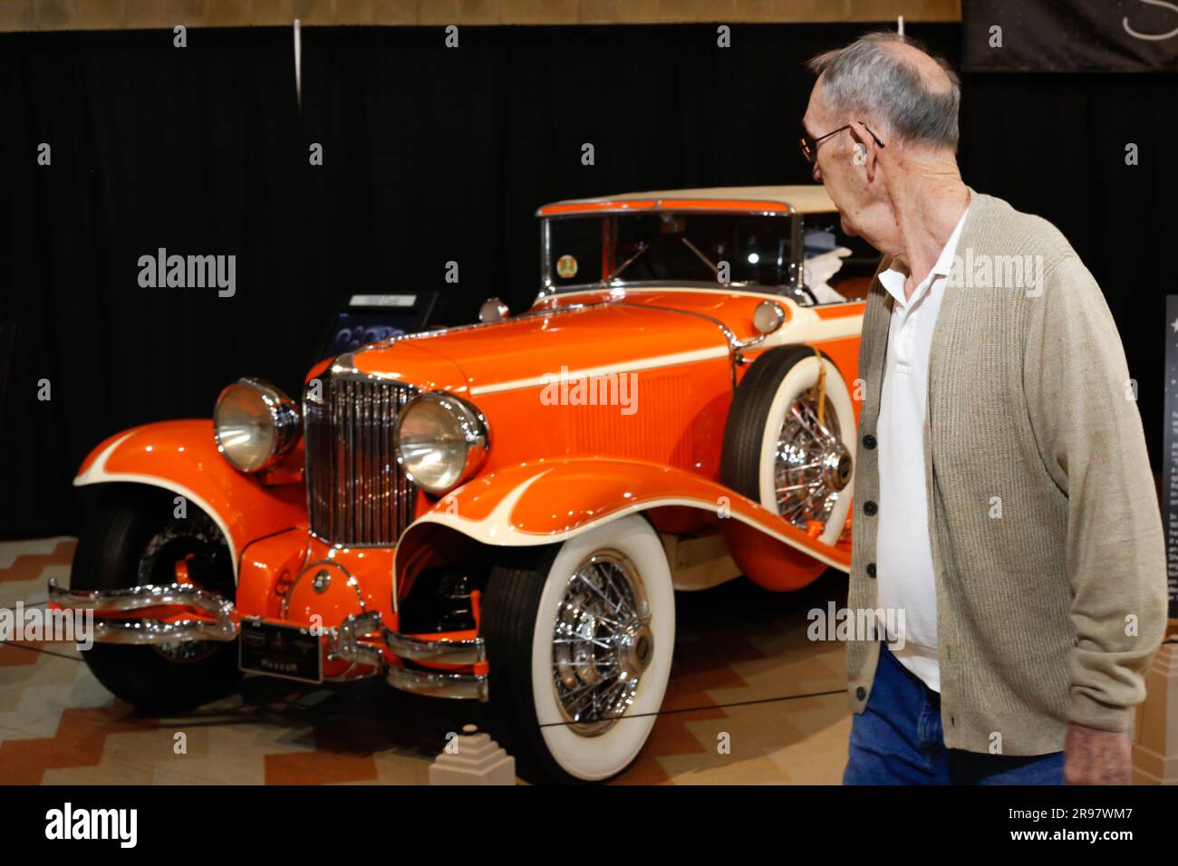An elderly man looks back at a historic orange 1930 Cord L-29 Cabriolet on display at the Auburn Cord Duesenberg Museum in Auburn, Indiana, USA. Stock Photo