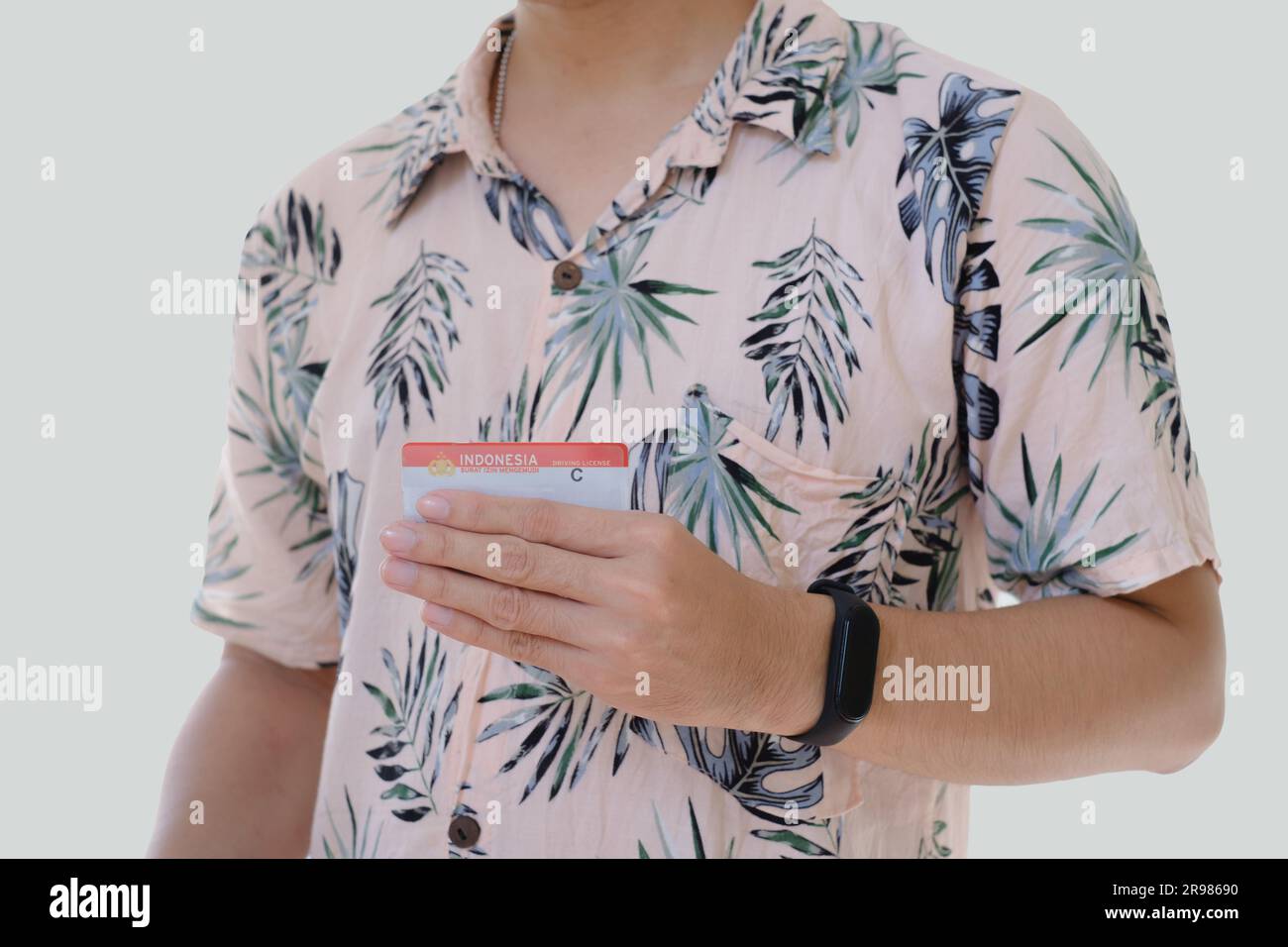 An Asian man wearing a pink shirt with tropical patterns is holding Surat Ijin Mengemudi or SIM C means Indonesian Driving License for motorbike Stock Photo