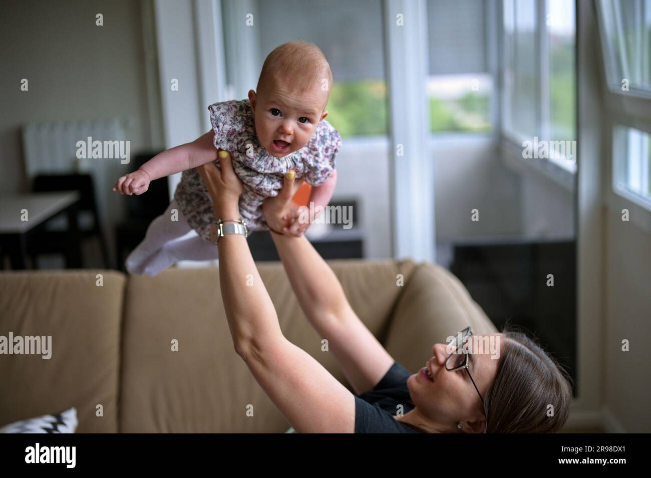 Mother sitting on a sofa and playing with cute little baby girl Stock ...