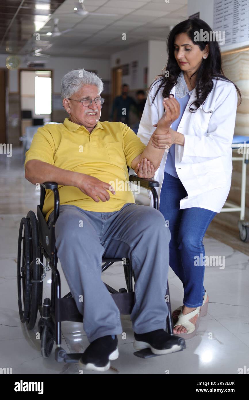 Indian Nurse looking very happy greeting a senior patient in a wheelchair at the hospital and smiling - healthcare concepts. Stock Photo