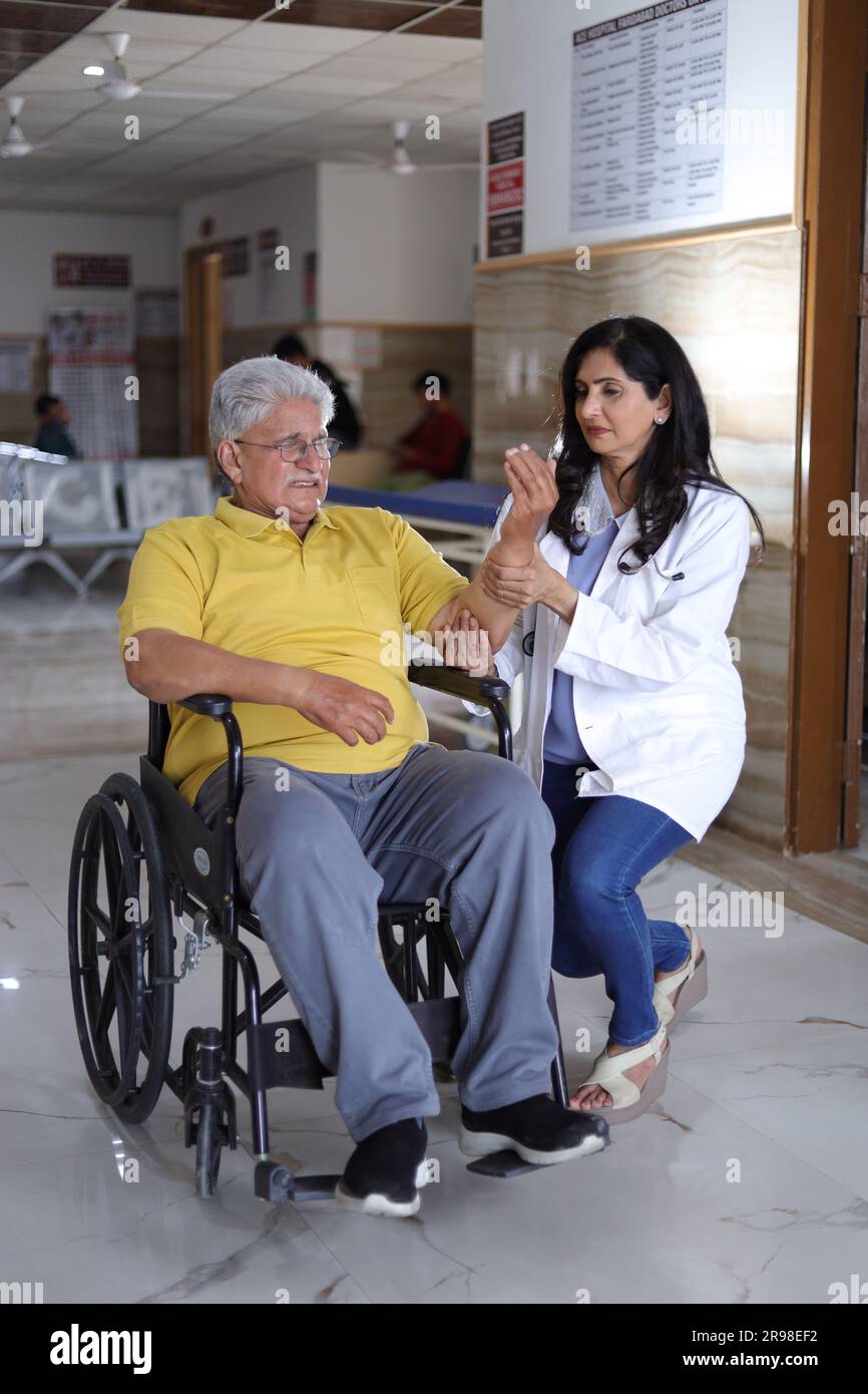 Indian Nurse looking very happy greeting a senior patient in a wheelchair at the hospital and smiling - healthcare concepts. Stock Photo