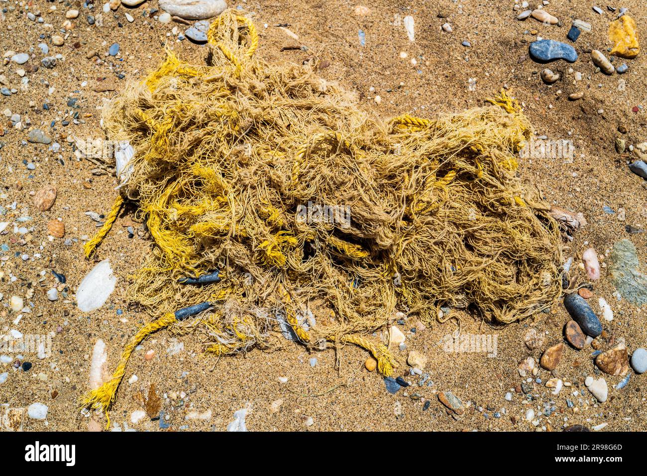 Tangled fishing net in the sand. Unnecessary trash polluting the environment. Symbol of ocean pollution. Ecological damage. Stock Photo
