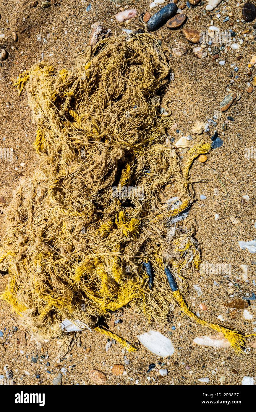 Tangled fishing net in the sand. Unnecessary trash polluting the environment. Symbol of ocean pollution Stock Photo