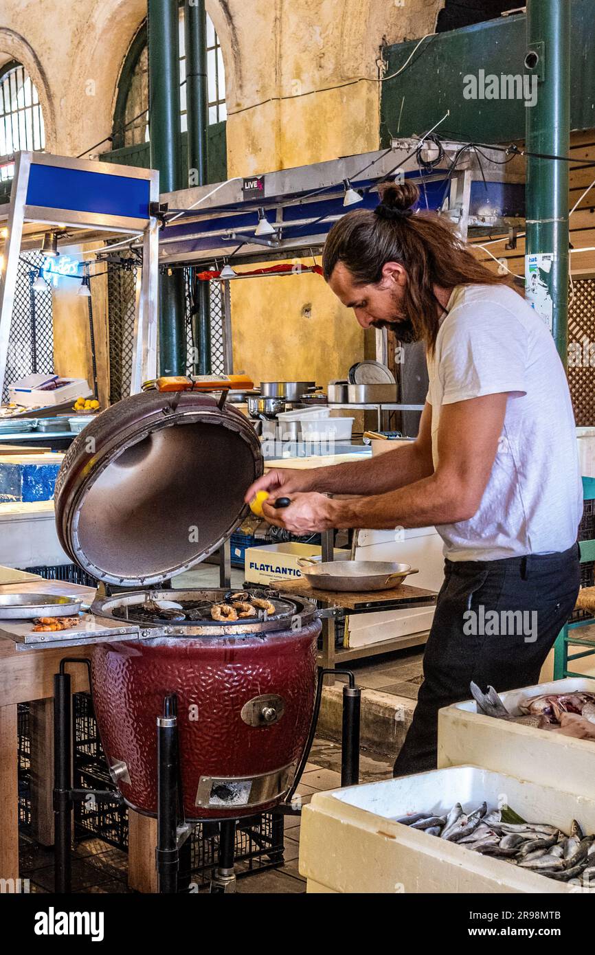 Streetfood fish stall in the central market of Athens, Greece. Cook preparing fresh fish for the charcoal grill. Pop-up streetfood. Stock Photo