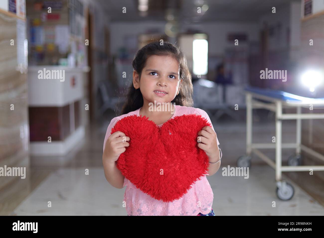 Small girl child showing red colored heart shaped cushion, standing in