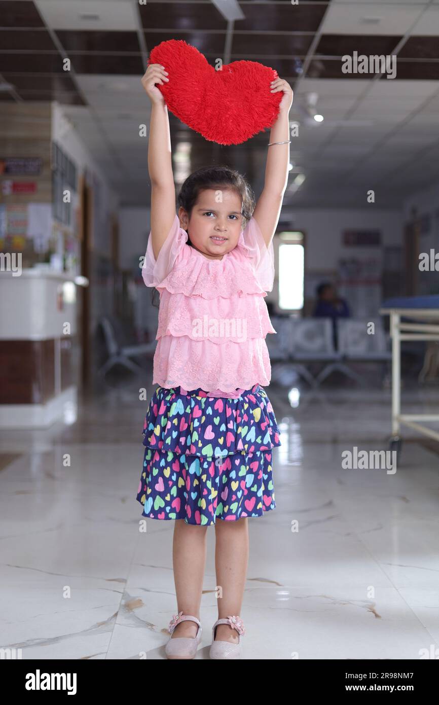 Small girl child showing red colored heart shaped cushion, standing in