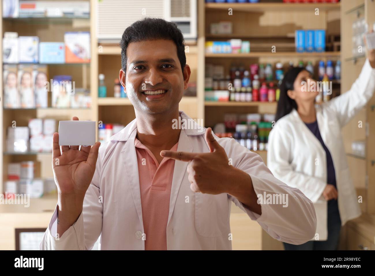 Pharmacist chemist woman standing in pharmacy - drugstore. Pharmacist assisting to customers in pharmacy Holding business card in hand. Stock Photo