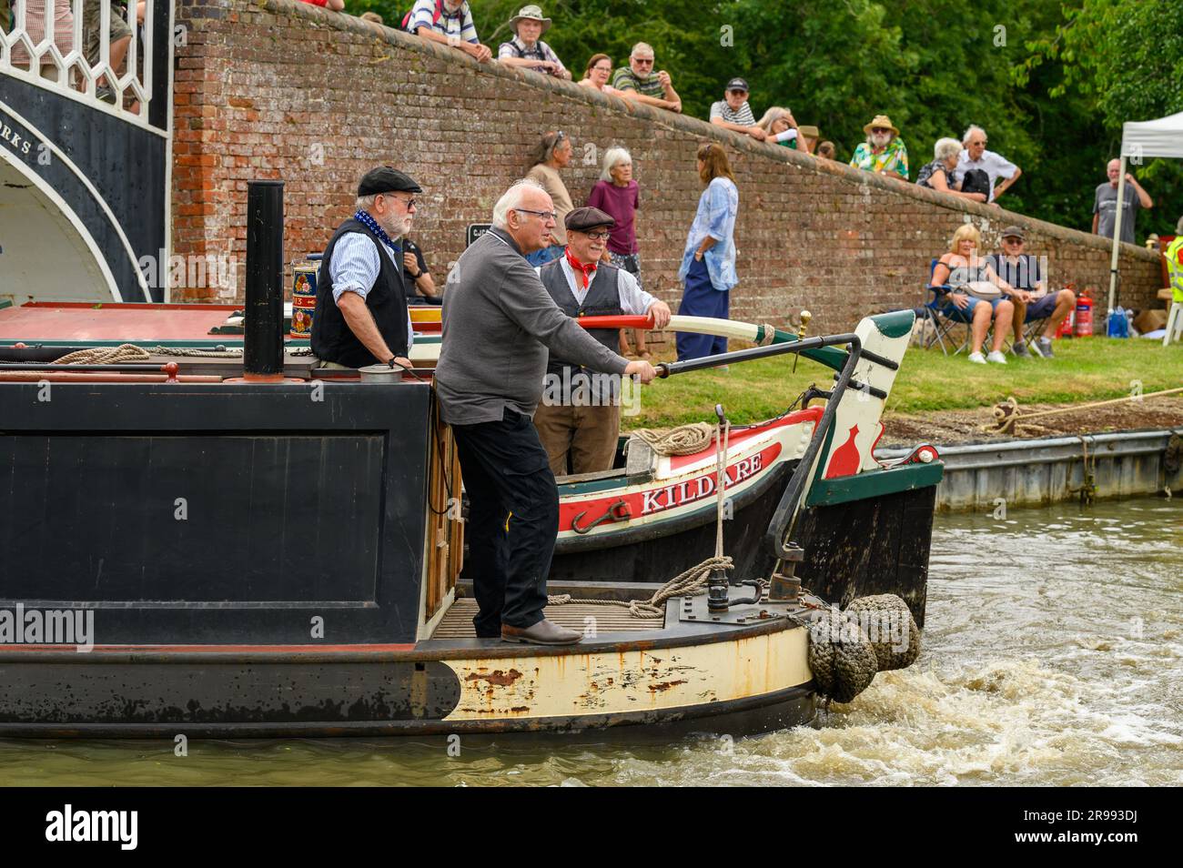 Braunston,  UK. 24th, June, 2023. Pete Waterman OBE DL, long-standing supporter of the waterways and steam trains, takes the tiller of a steam powered narrowboat during the opening ceremony at the annual Braunston Historic Narrowboat Rally.. © Phil Pickin/ Alamy Live News Stock Photo