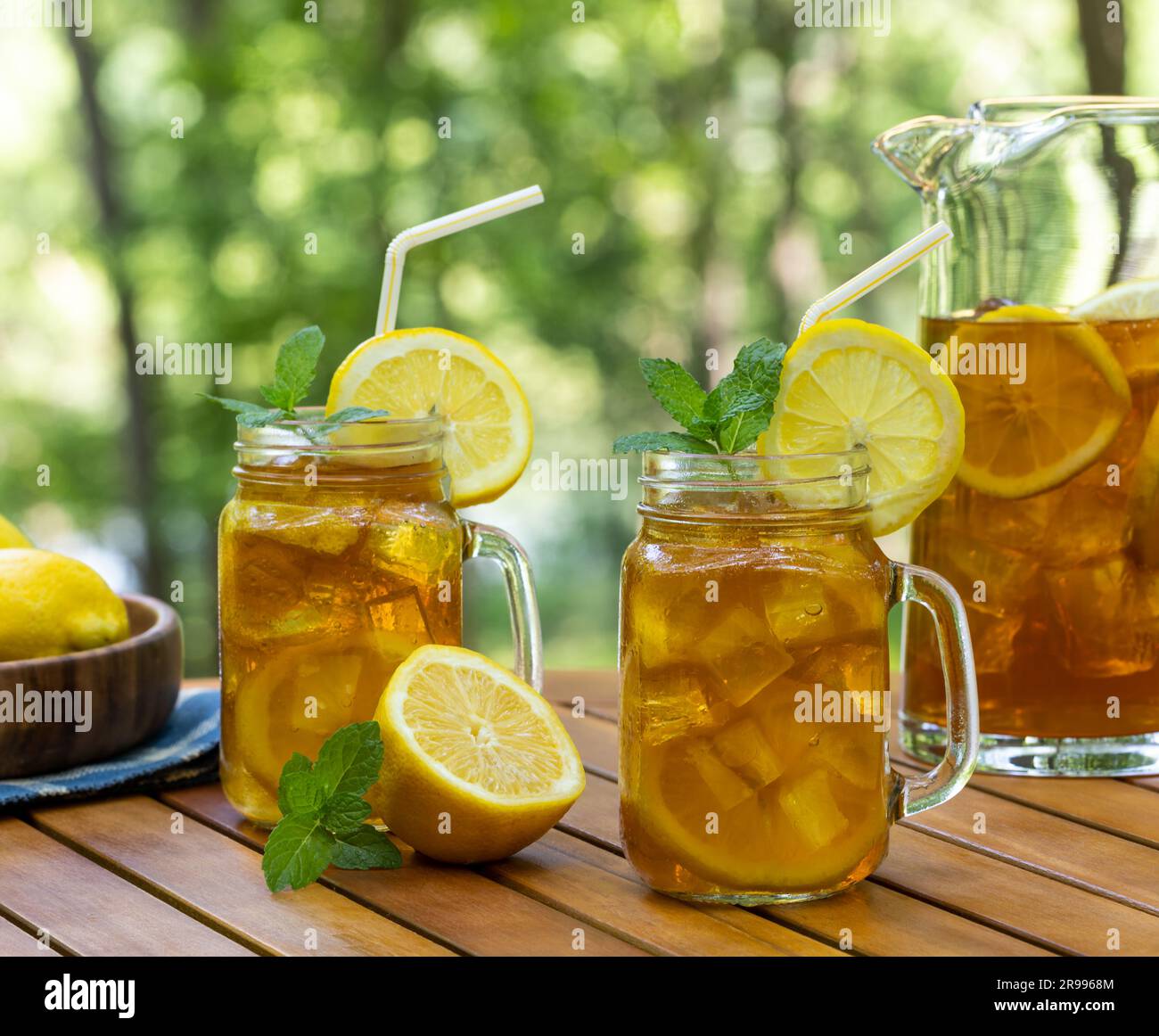 https://c8.alamy.com/comp/2R9968M/ice-tea-in-glasses-and-pitcher-with-lemon-and-mint-on-wooden-table-with-nature-background-2R9968M.jpg