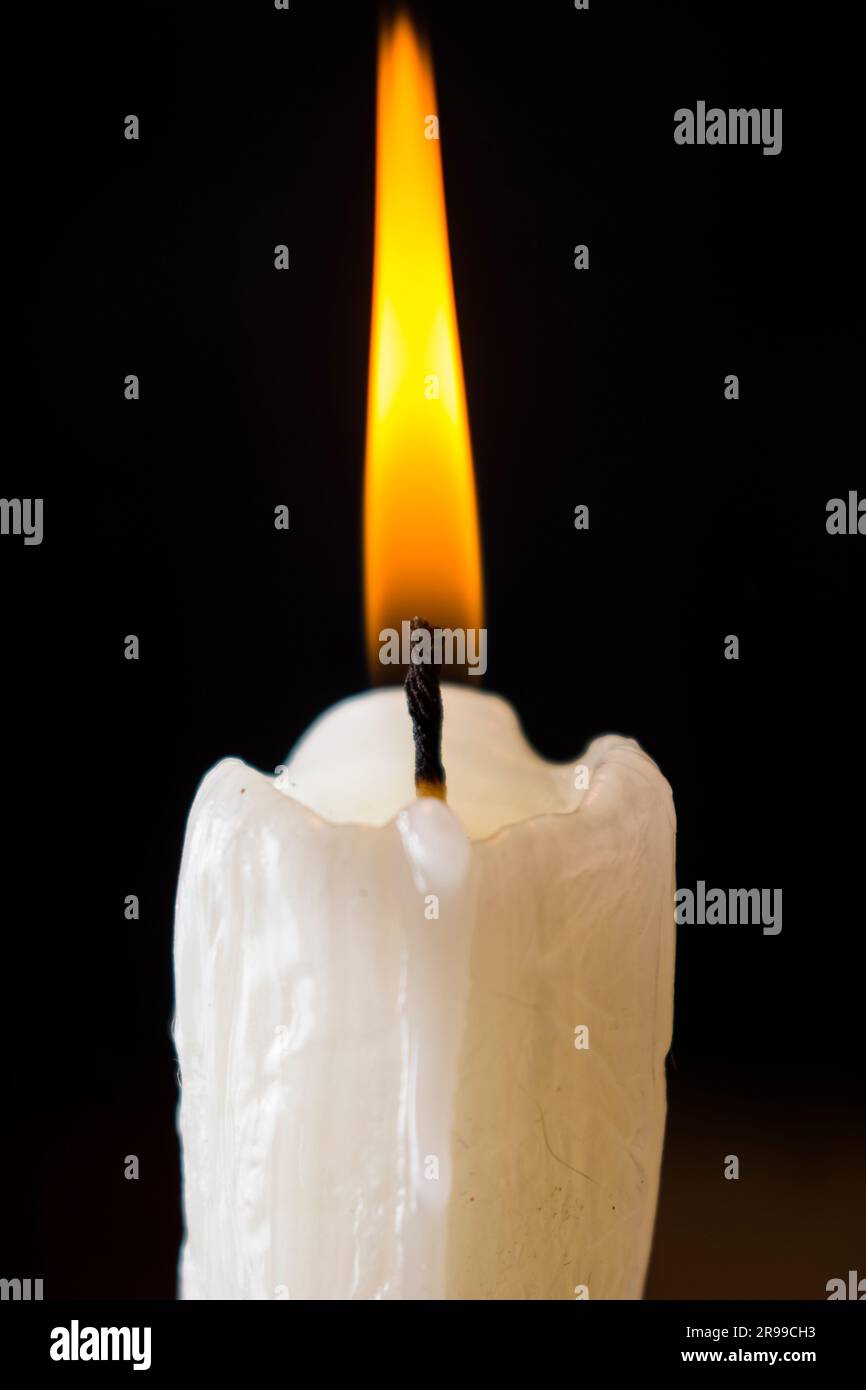 White candle burning with yellow fire on a black background Stock Photo