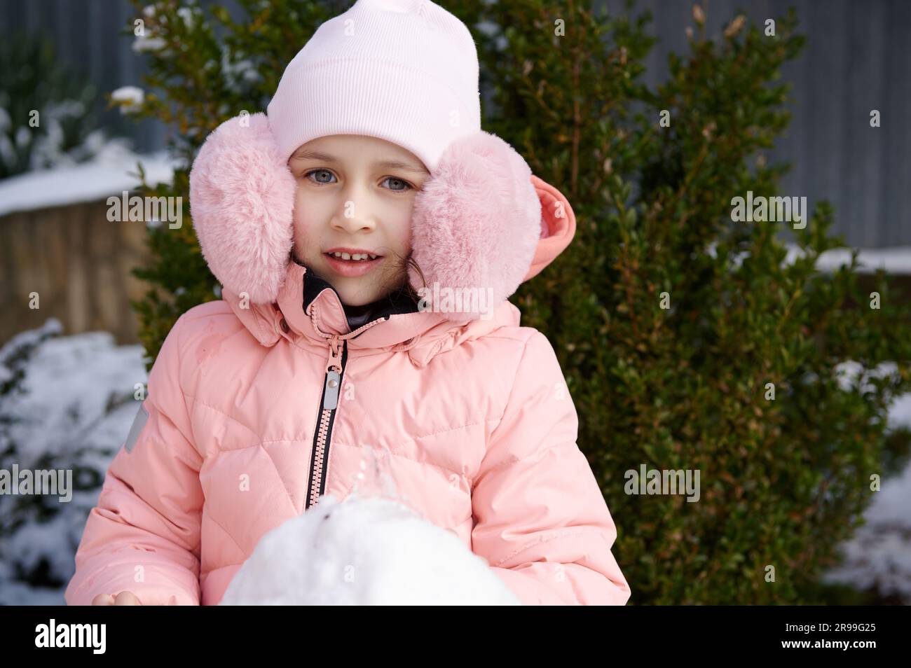 Beautiful little girl in pink fluffy ear muffs and down jacket, smiling