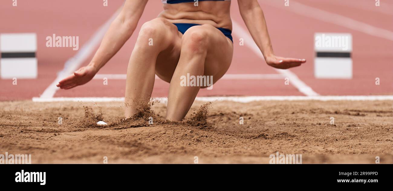 Female athlete long jump landing sand spray, landing in long jump in