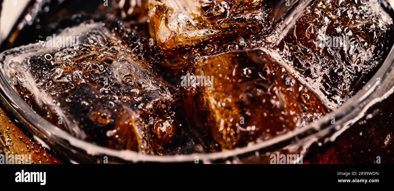 Cola with Ice. Close up of the ice cubes in cola water. Texture of carbonate drink with bubbles in glass. Cola soda and ice splashing fizzing or float Stock Photo