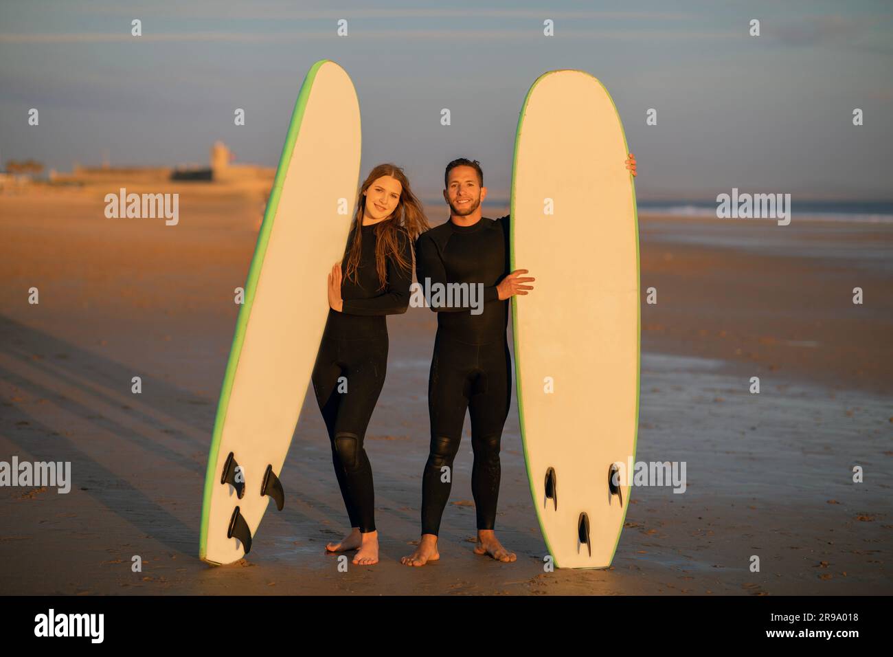 Happy Young Couple Posing With Their Surfboards On The Beach At Sunset Stock Photo
