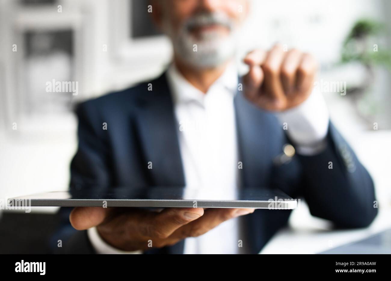 Serious handsome mature european man with beard in suit works, use tablet in office interior, close up Stock Photo