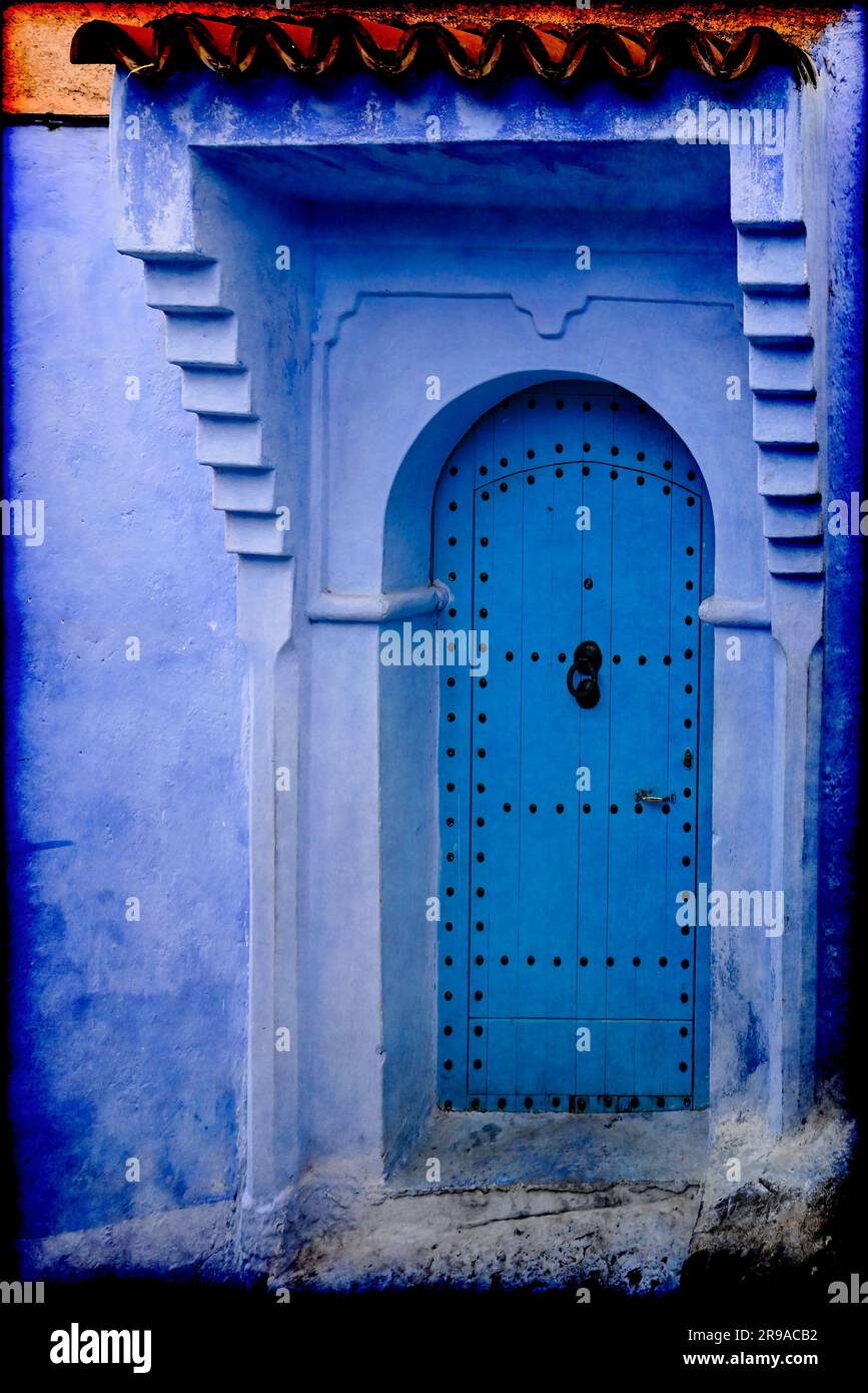 An exterior wall and a formidable arched wooden front door are shades of blue, well representing the Blue City, ancient Chefchaouen, Morocco Stock Photo