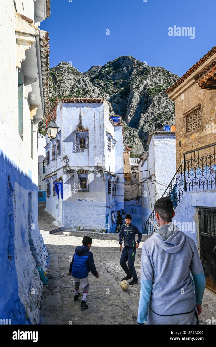 Three young males play football (soccer) in the narrow streets of a village in the Riff Mountains in Northwest Morocco, The Blue City, Chefchaouen Stock Photo