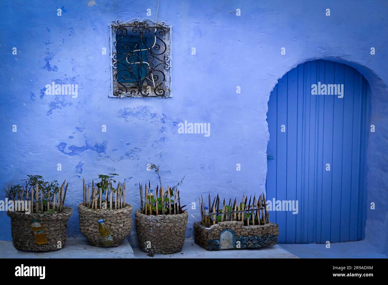 A mesmerizing ancient blue home with a blue door and rock planters with  deterrent spikes in Moroccan traditional architecture in Chefchaouen, Morocco Stock Photo
