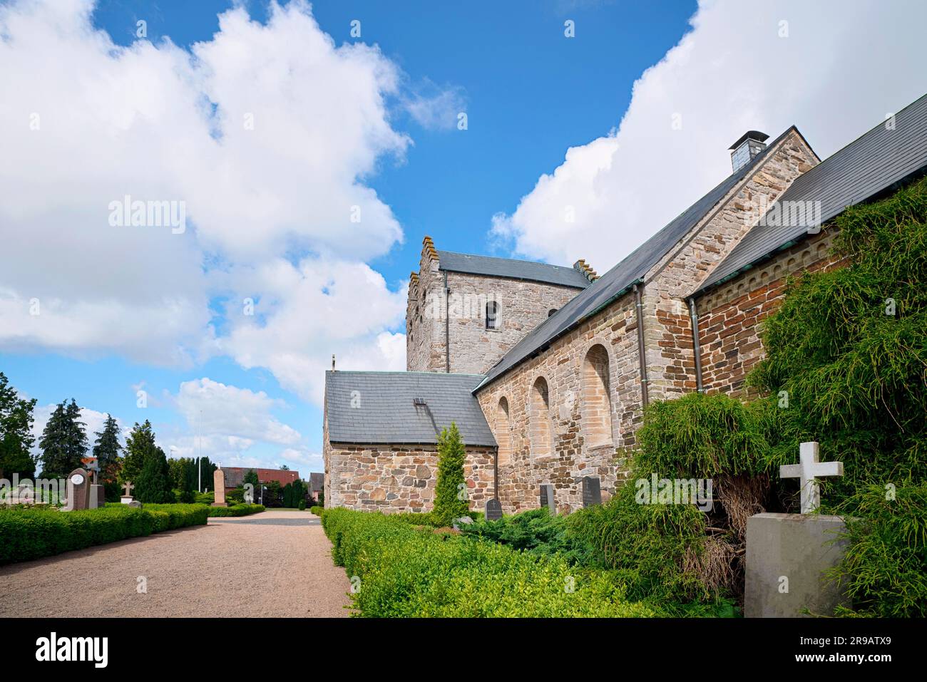 Tombstone with a cross in front of a church under a blue sky in the daytime Stock Photo