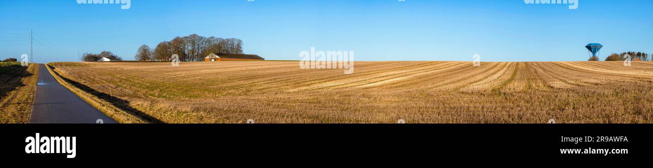 Rural panorama landscape with a dry field under a blue sky with a water tower on the right side Stock Photo