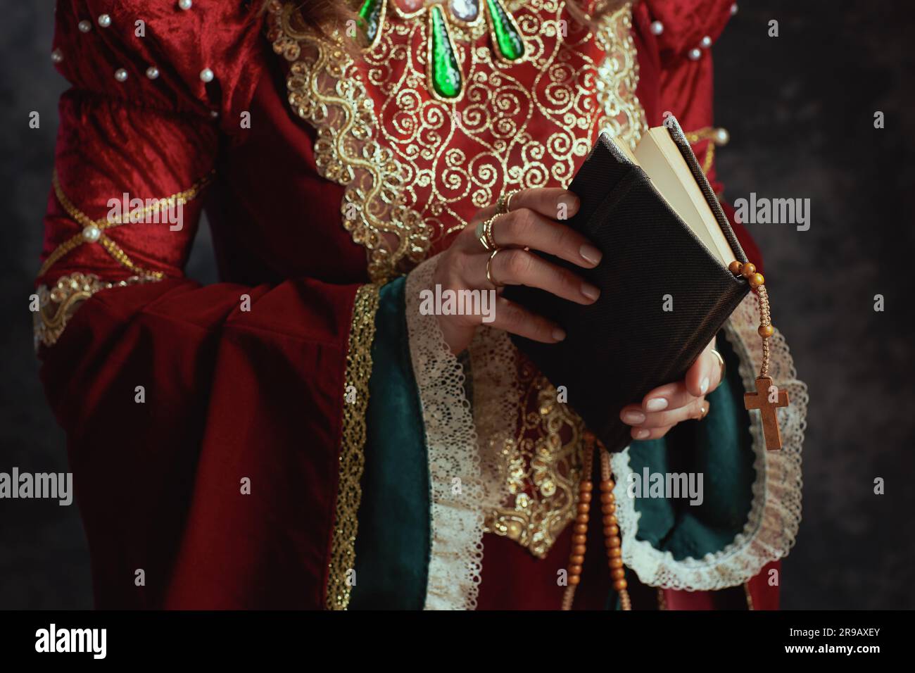 Closeup on medieval queen in red dress with book and rosary on dark ...