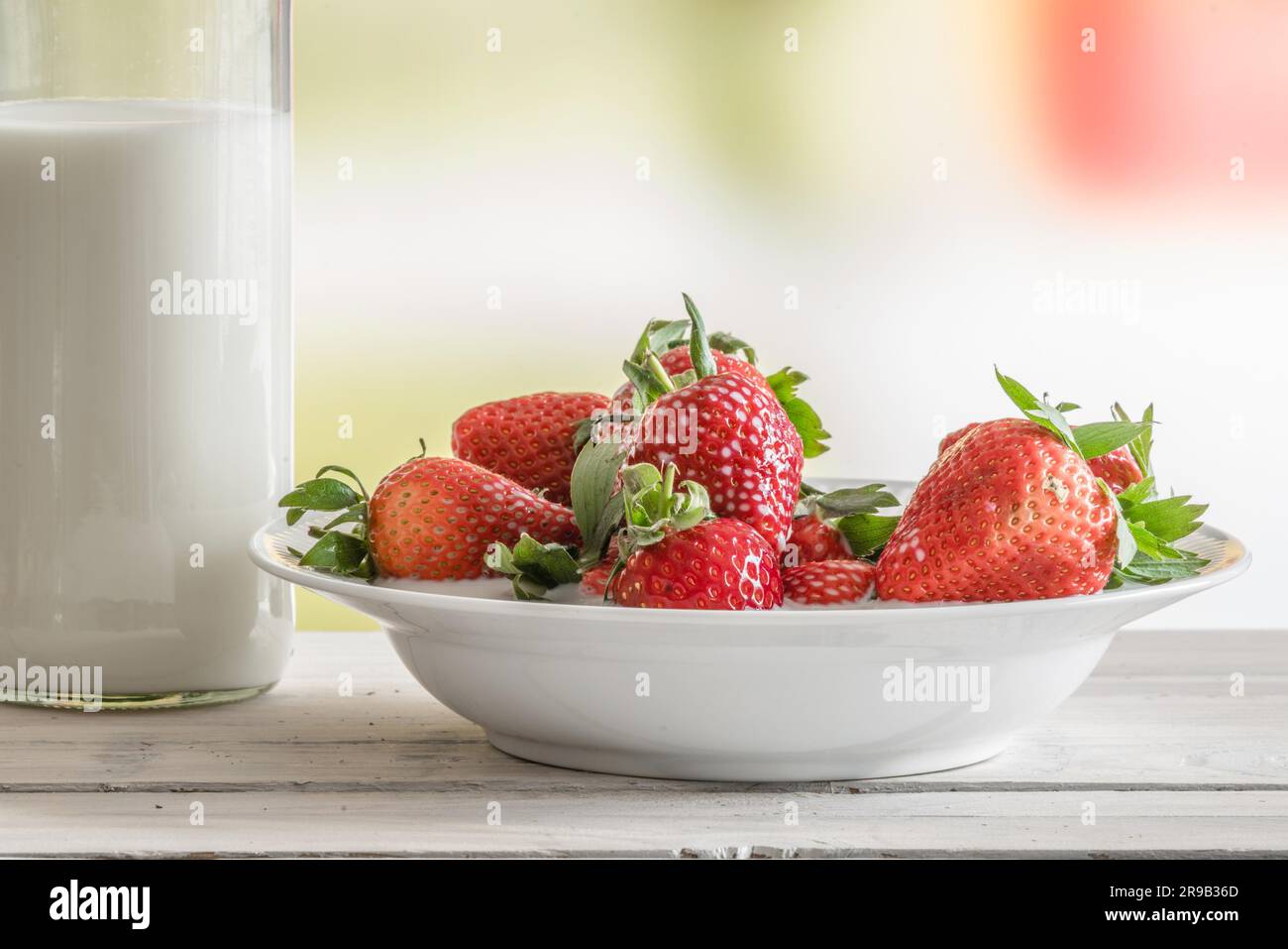 Strawberries on a plate with a bottle of milk on a table Stock Photo