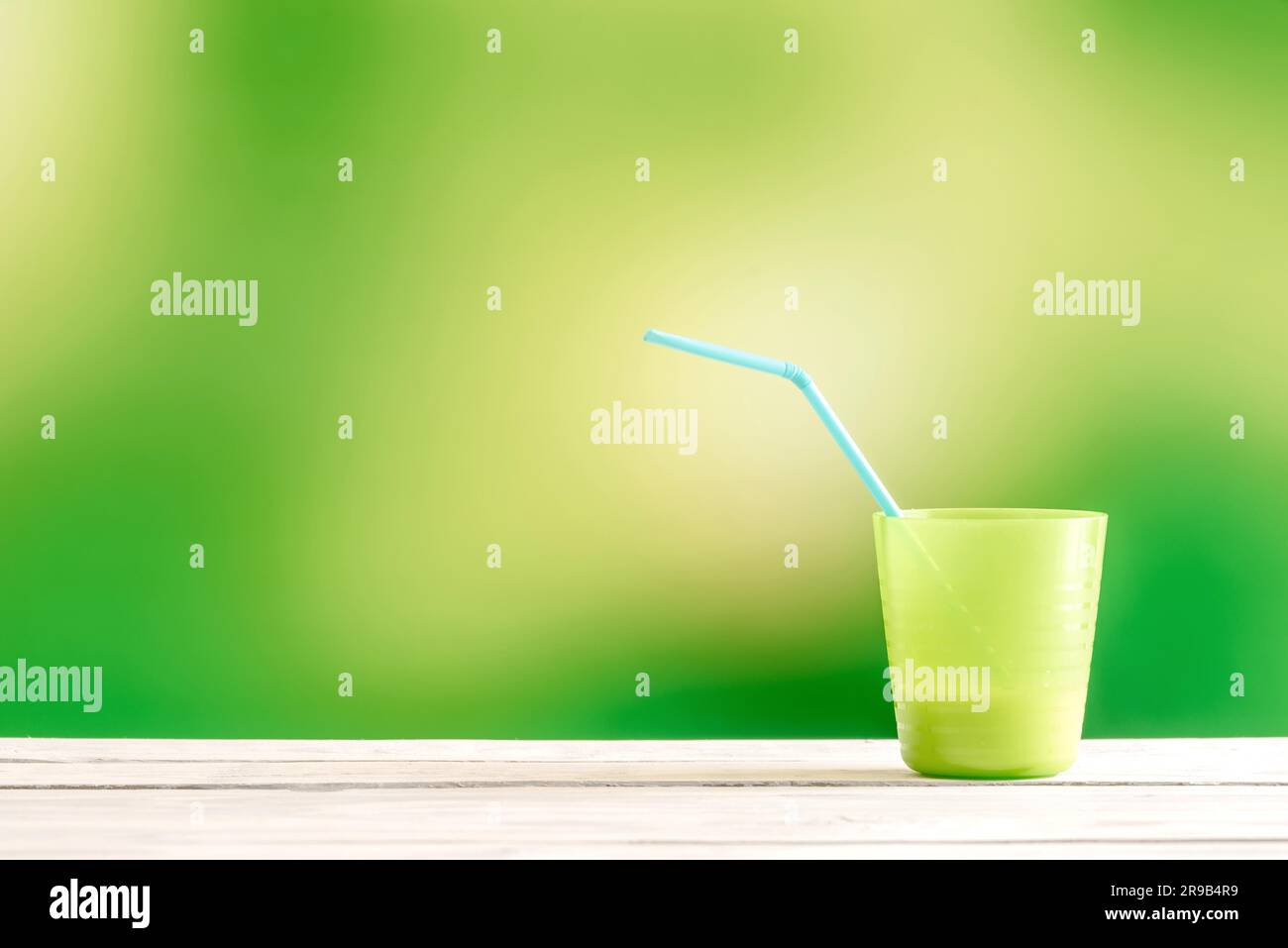 Green cup with a blue straw on a wooden table Stock Photo